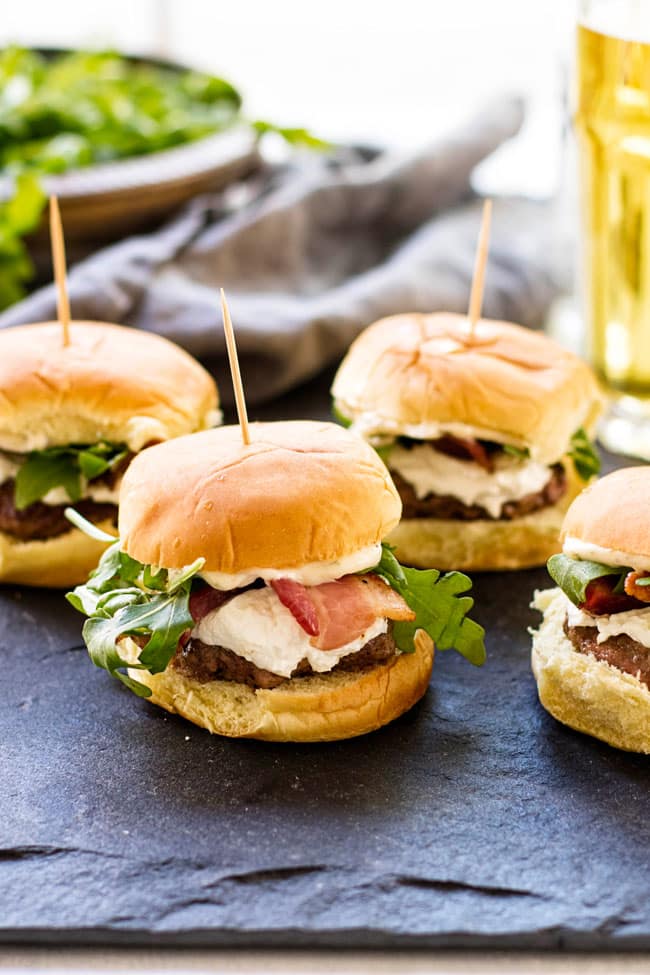 Four goat cheese and bacon sliders with a napkin and a glass of beer