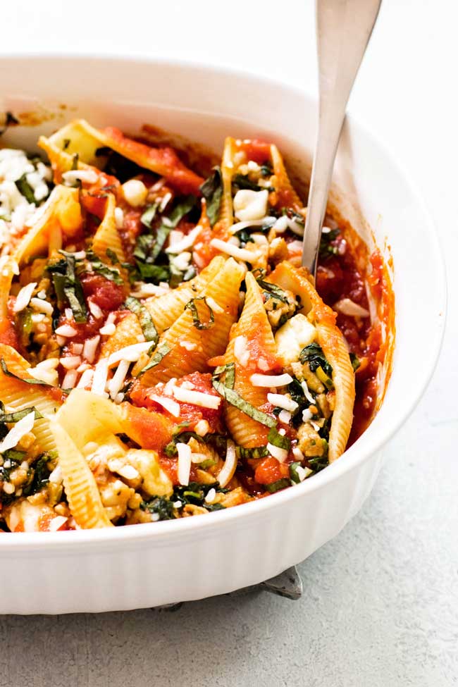 Chicken-basil baked shells in a baking dish with a serving spoon