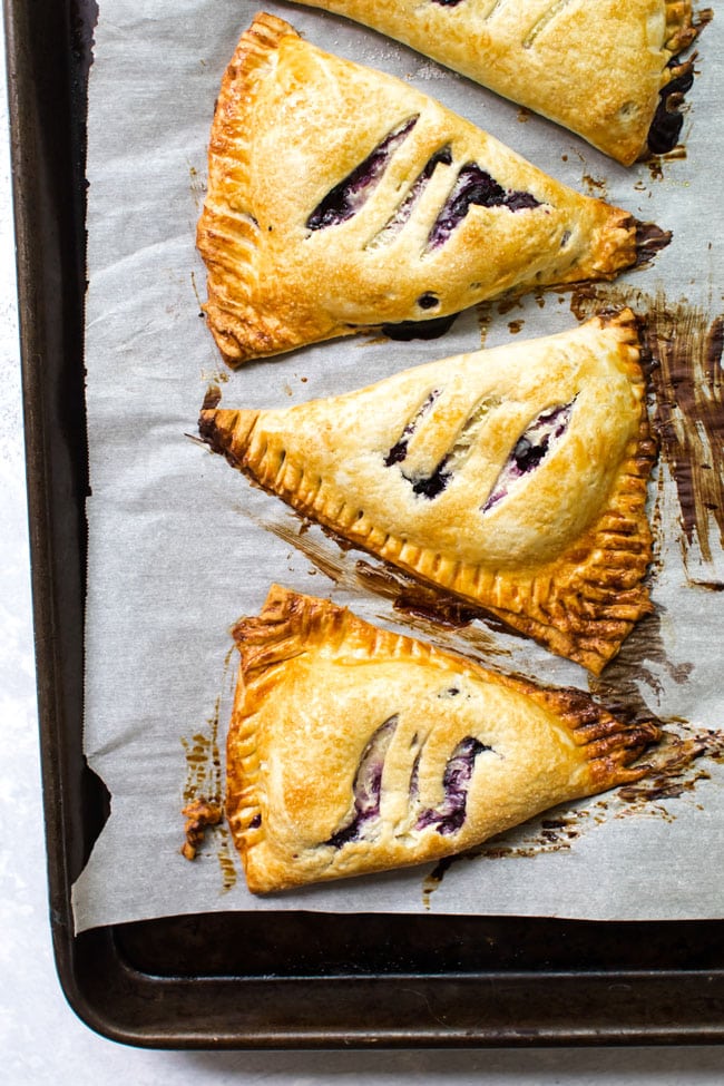 Three blueberry hand pies on a baking sheet lined with parchment paper