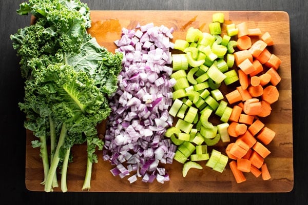 Raw kale, onion, celery, and carrots on a cutting board