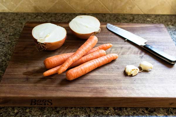 raw carrots, onion, and garlic on a wooden cutting board