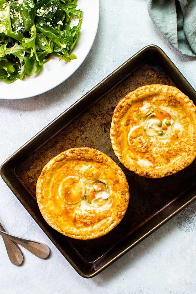 Two chicken pot pies on a baking sheet with a green salad