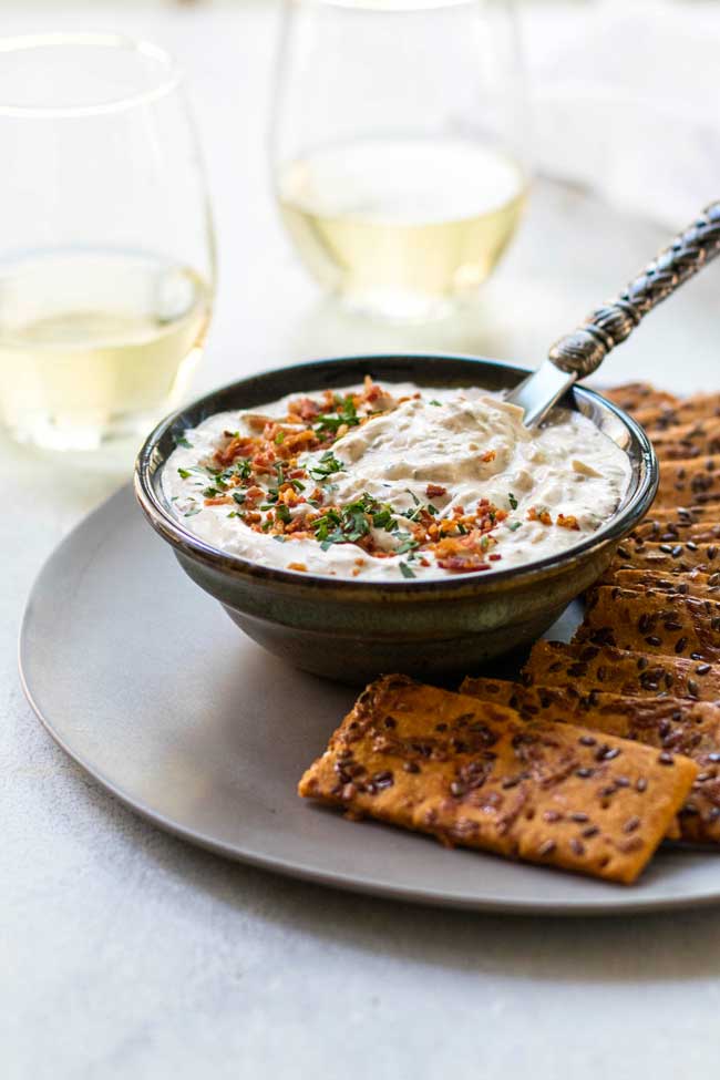 A bowl of onion dip on a plate with roasted red pepper crackers