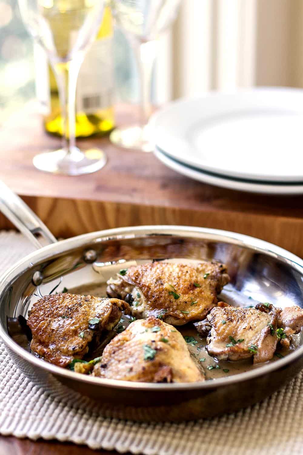 Chicken thighs in a skillet with rosemary wine sauce with white plates in the background