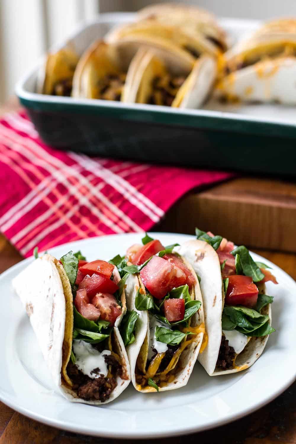 Baked double decker tacos on a white plate with a baking dish in the background