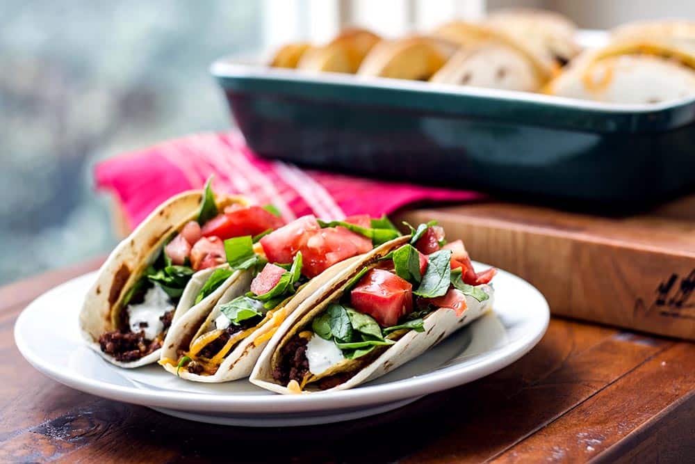 Three baked double decker tacos on a plate topped with lettuce and tomatoes