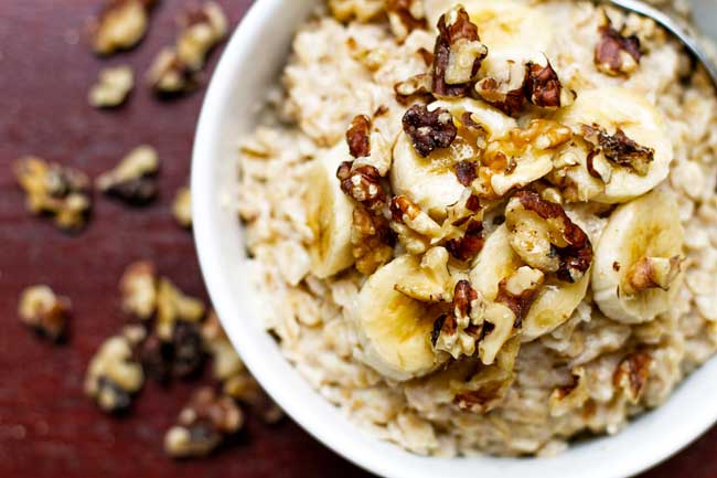 a bowl of banana nut oatmeal topped with nuts and banana slices