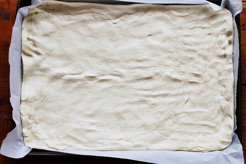 Foccacia dough stretched into a baking sheet lined with parchment