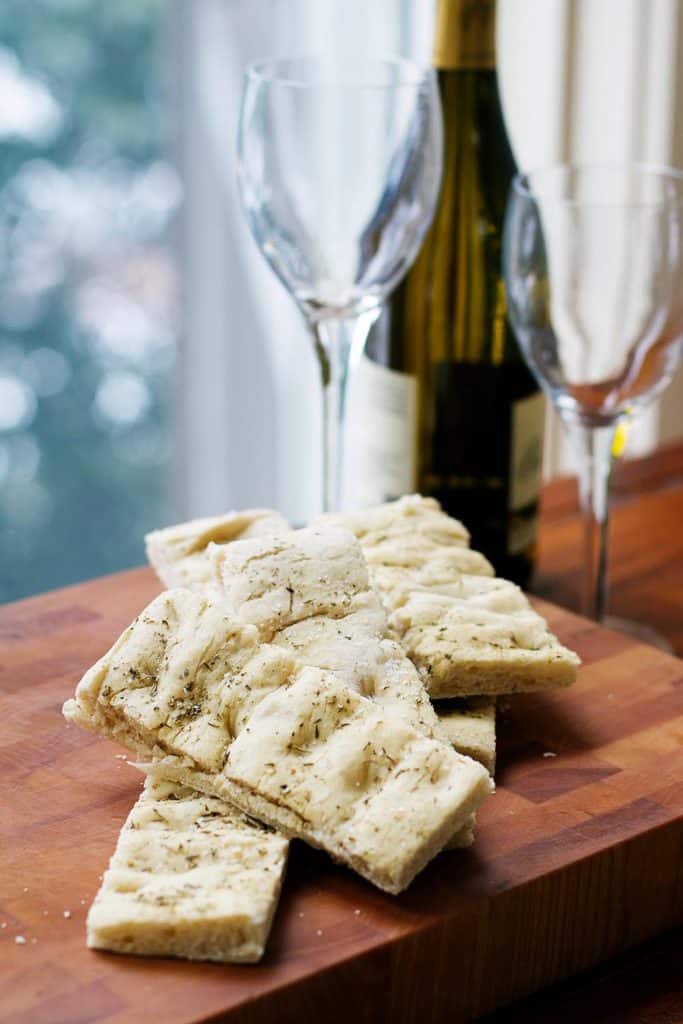 Foccacia on a cutting board with a wine bottle and glasses