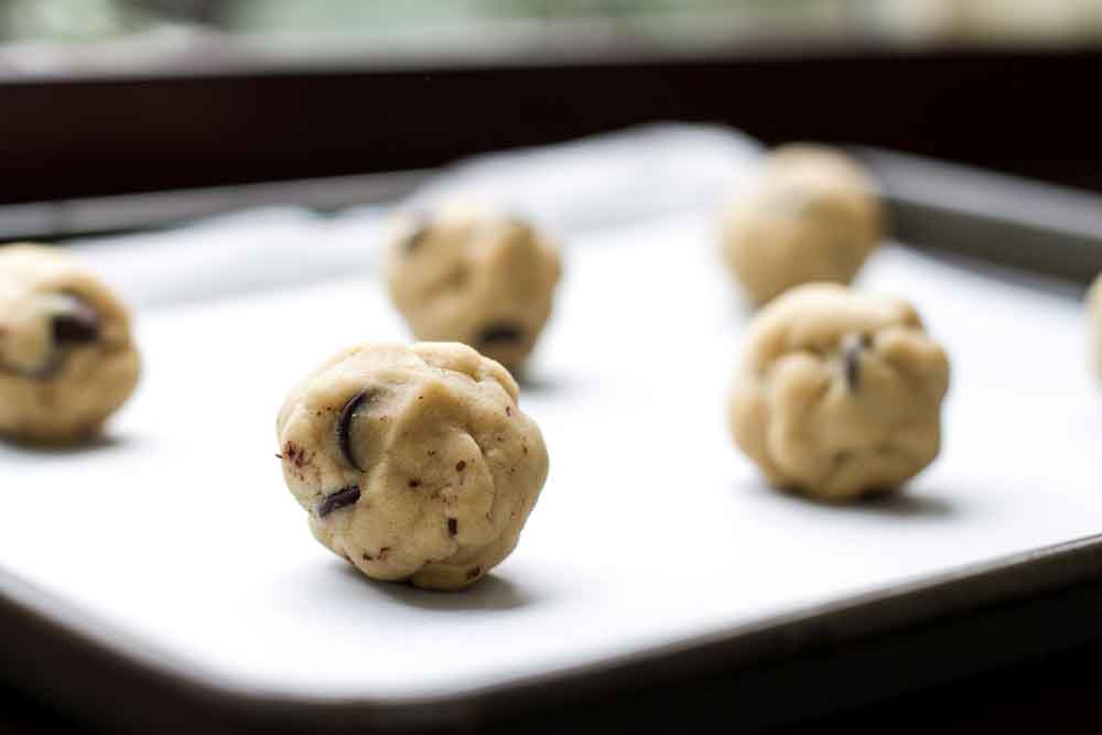 Chocolate chip cookie dough balls lined up on a baking sheet