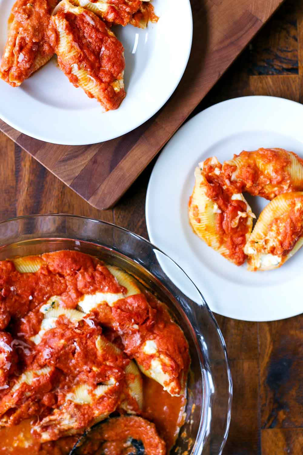 Baked stuffed shells in a baking dish with two white plates with one serving each