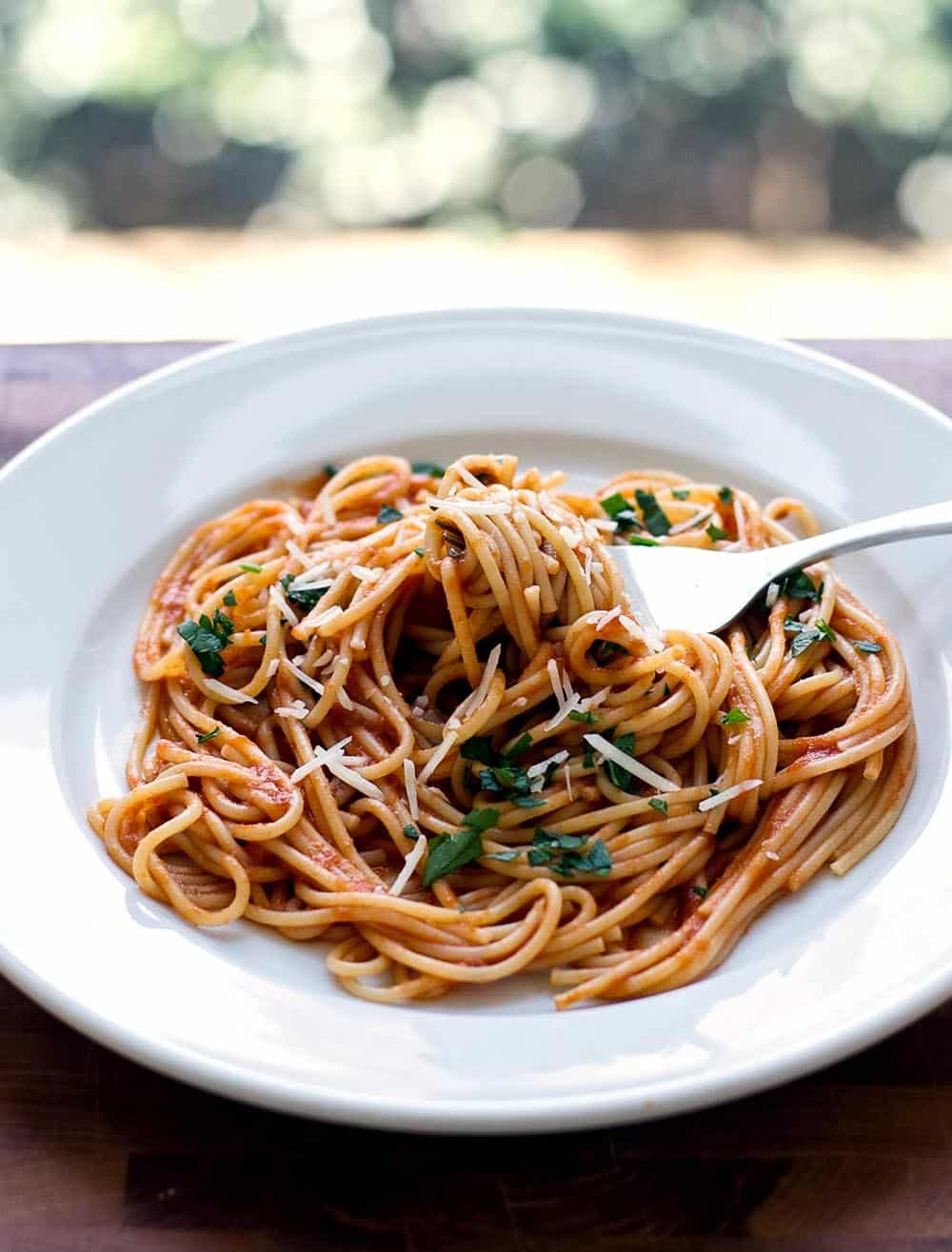 Pasta with oven tomato sauce on a white plate with fresh herbs and a fork.