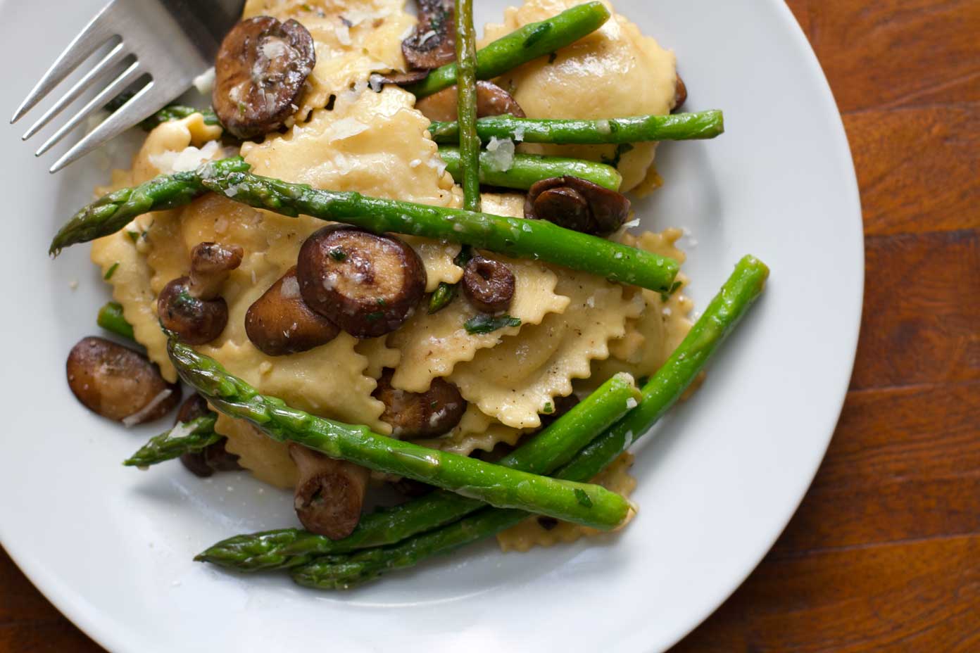 20-minute ravioli with asparagus and mushrooms on a white plate with a fork