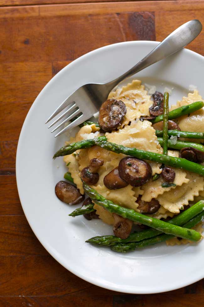 Ravioli with asparagus and mushrooms on a white plate with a fork