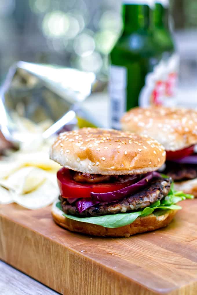 two black bean burgers with potato chips and bottle of beer in the backrgound