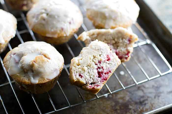 raspberry muffins on a baking sheet with one muffin sliced in half