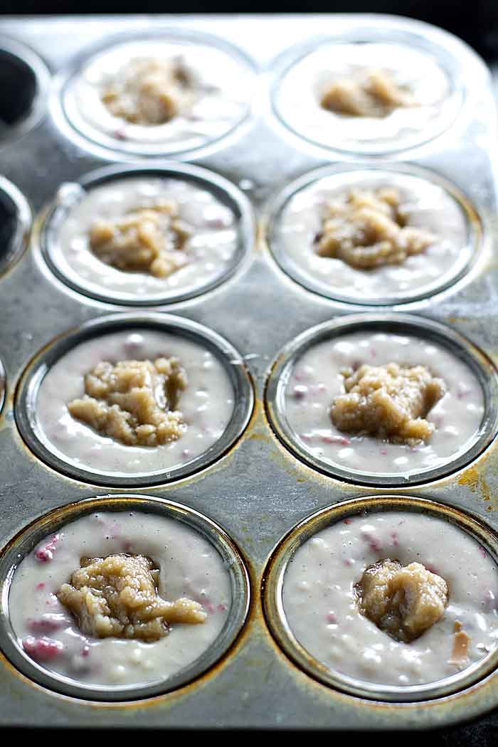 raspberry muffin batter with streusel in the middle in a muffin tin ready to be baked