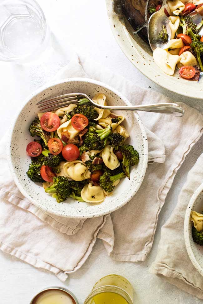 one serving of tortellini pasta salad in a bowl on a tan napkin