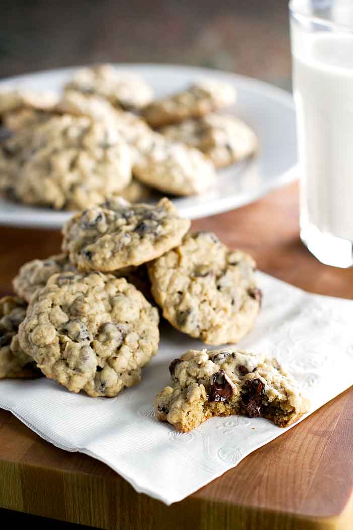 a pile of oatmeal raisin cookies with chocolate chips on a napkin with one cookie with a bite taken out