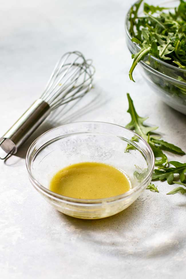 Dijon dressing in a small clear glass bowl that is tossed with the roasted sweet potato and arugula salad