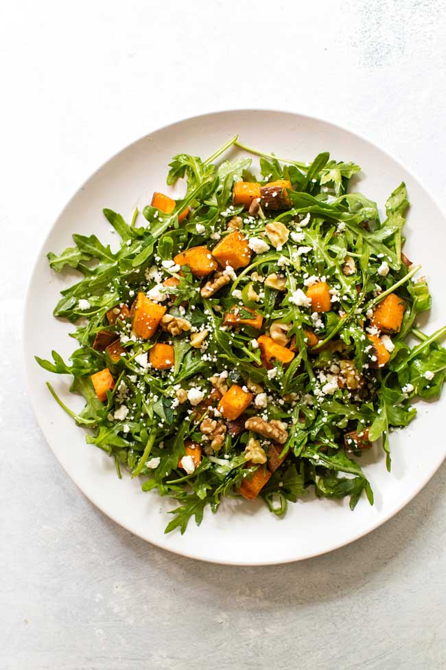 roasted sweet potato and arugula salad on a large white plate