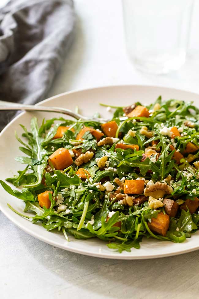 roasted sweet potato and arugula salad on a plate with a grey napkin and water glass in the background