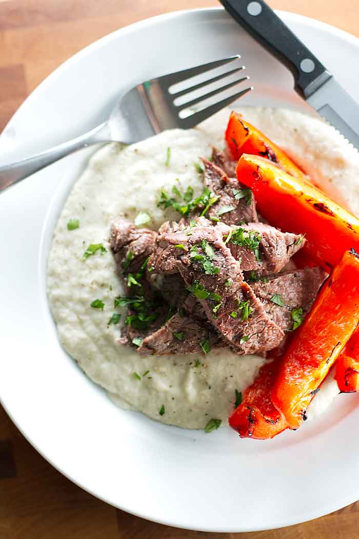 Eggplant puree, grilled steak, and bell peppers on a plate with a knife and fork