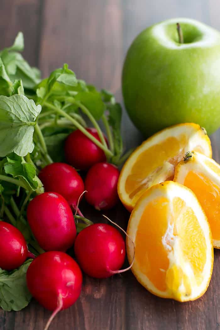 fresh radishes with orange segments and a green apple in the background