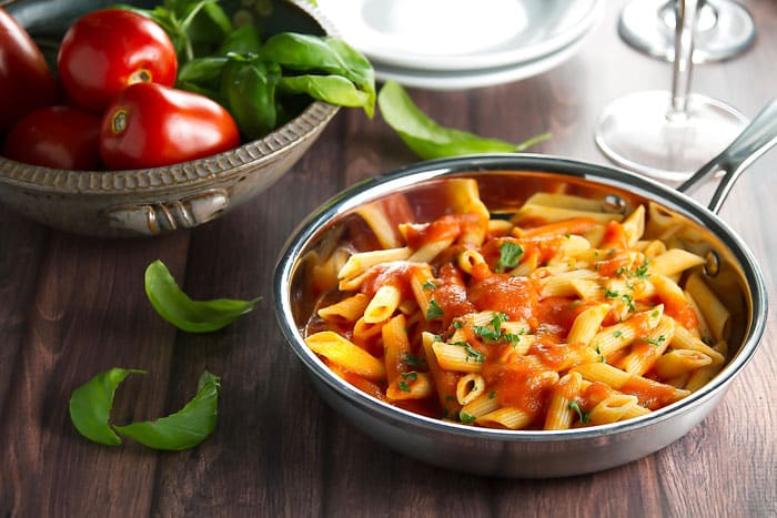 pasta with pomodoro sauce in a skillet with fresh tomatoes and basil in a bowl