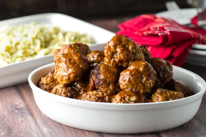 Braised Meatballs in a white dish with buttered noodles in the background