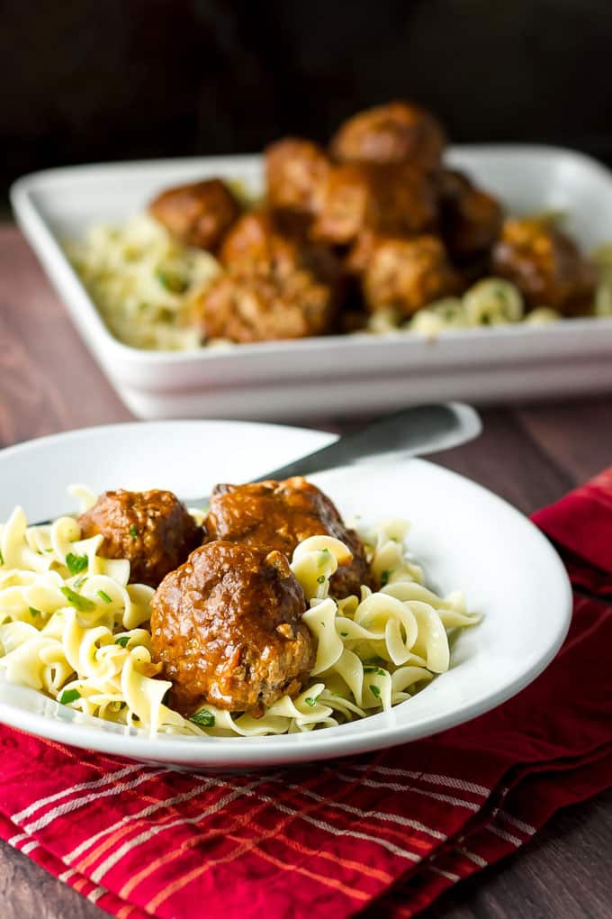 buttered noodles topped with braised meatballs in a white bowl