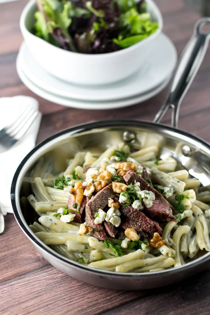 blue cheese pasta with steak in a skillet with a salad in the background