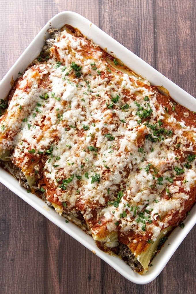 Baking dish with cheesy beef manicotti topped with sauce and melted cheese