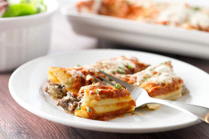 Baked cheesy beef manicotti on a white plate with a fork