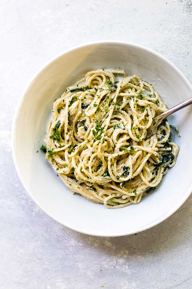 one serving of spaghetti with creamy goat cheese sauce in a white bowl with a fork