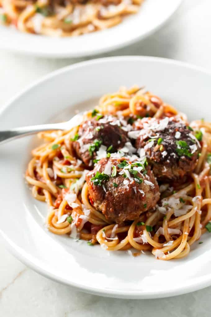 Spaghetti and Meatballs on a white plate garnished with parsley and cheese