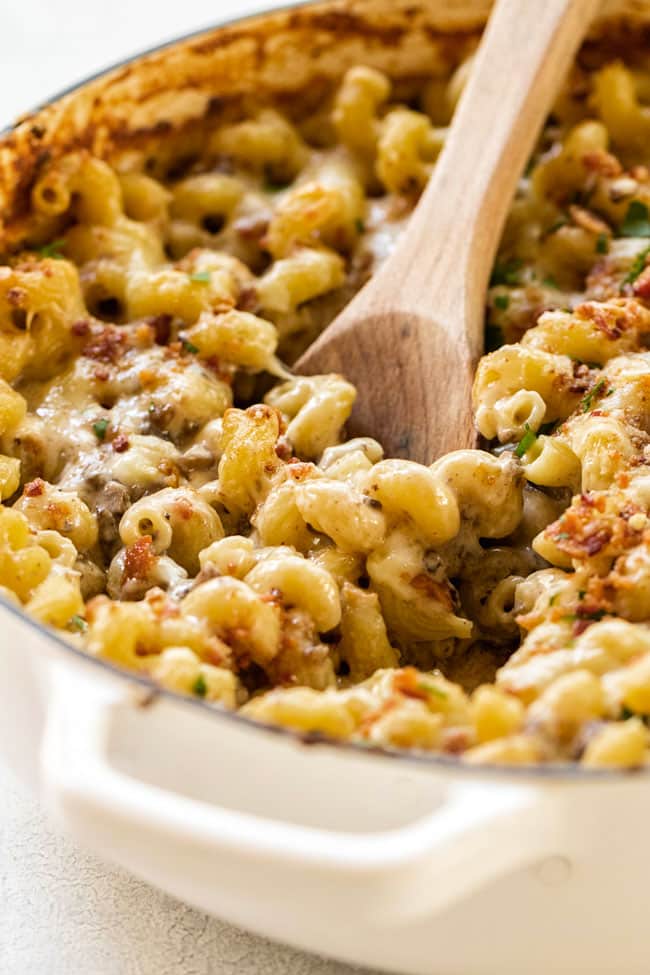 Creamy mushroom macaroni and cheese in a large pan with a wooden spoon