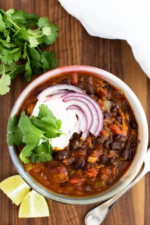 a bowl of black bean chili garnished with onions, sour cream, and fresh cilantro