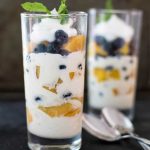 Ice cream layered in a glass with peaches, blueberries, and peach wine syrup. Garnished with whipped cream and mint
