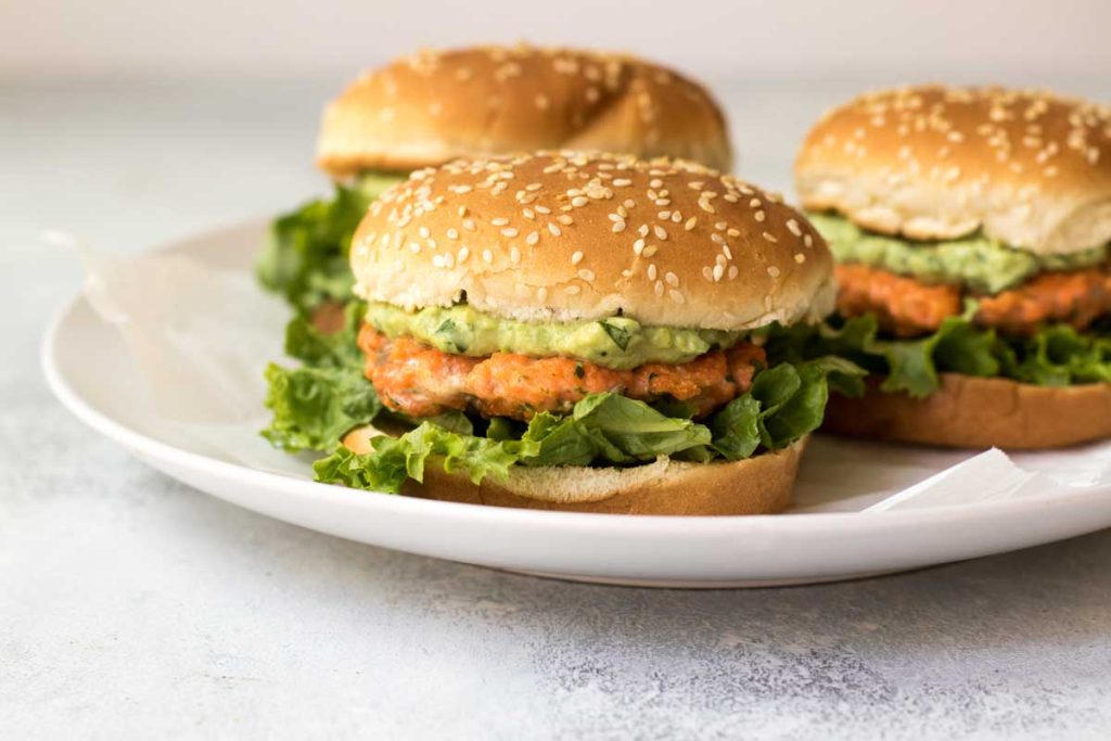 Salmon burgers with avocado mayo and lettuce on a white plate