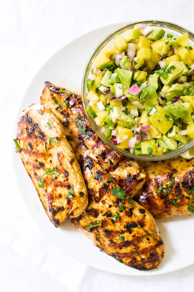 overhead photo of grilled chicken with a bowl of mango avocado salsa