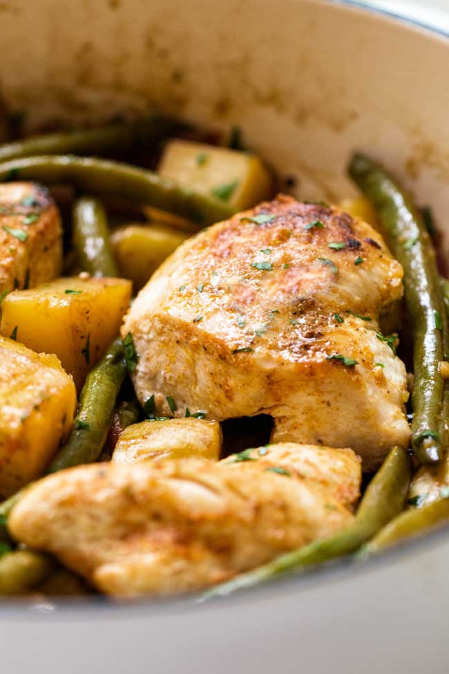 close-up photo of a piece of chicken in a pan with green beans and potatoes