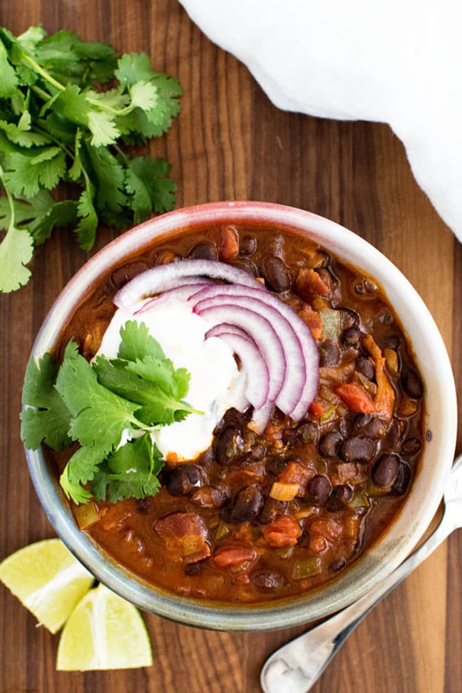 A bowl of black bean chili topped with sliced red onion and cilantro leaves
