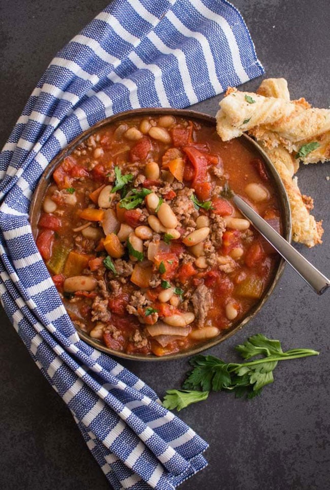 A big bowl of chili with beans with a napkin wrapped around the bowl