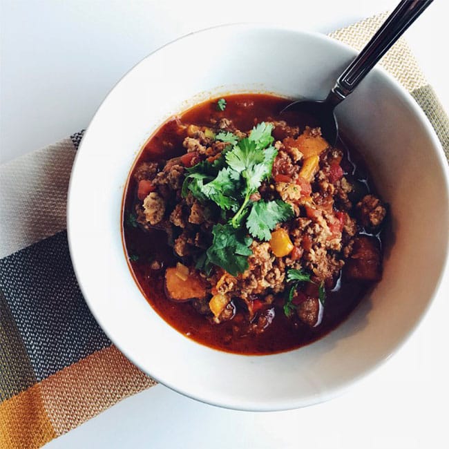 A white bowl and spoon with butternut squash chili