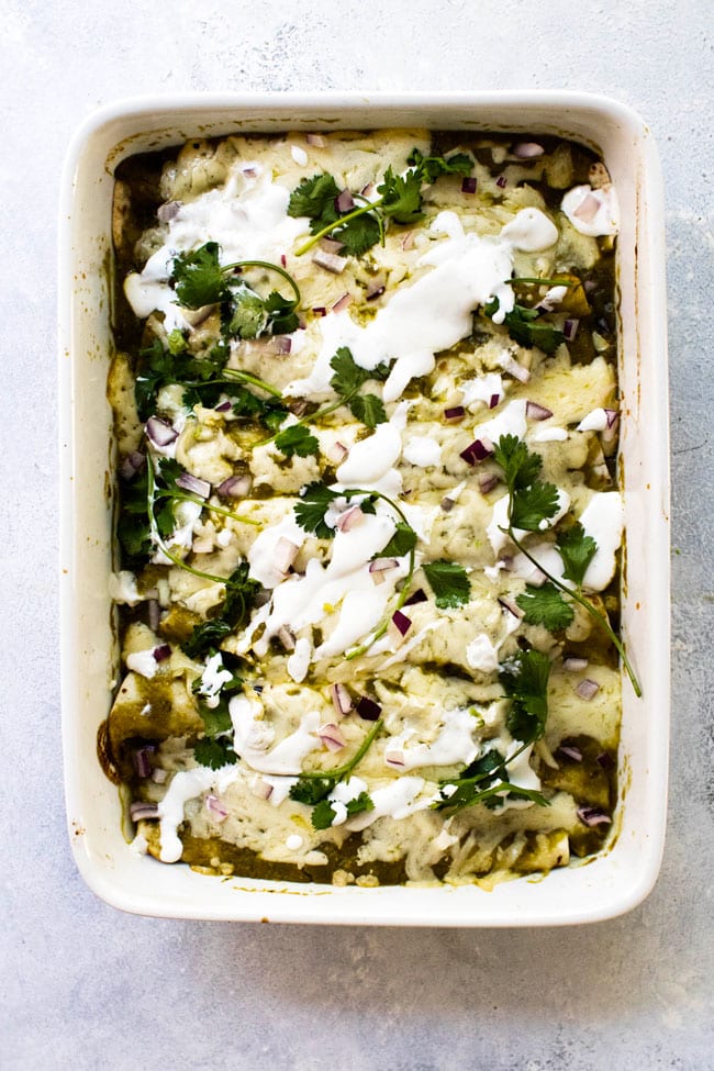 Chicken enchiladas in a baking dish topped with sour cream sauce and fresh cilantro