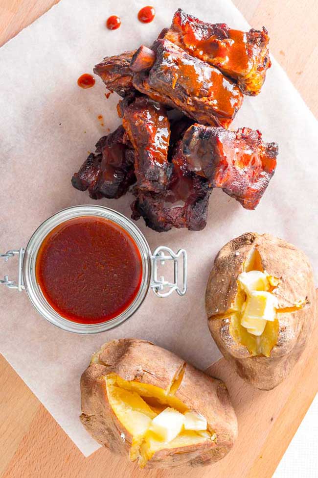 Char Siu Pork ribs on a board with extra sauce and baked potatoes on the side