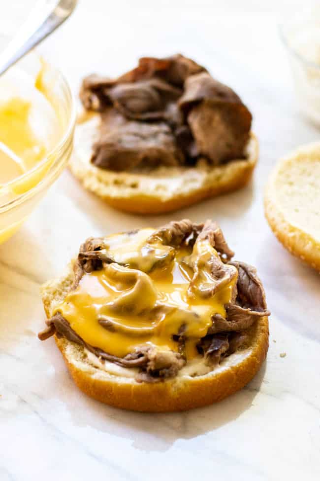 a hamburger bun with hot roast beef topped with creamy cheddar cheese sauce