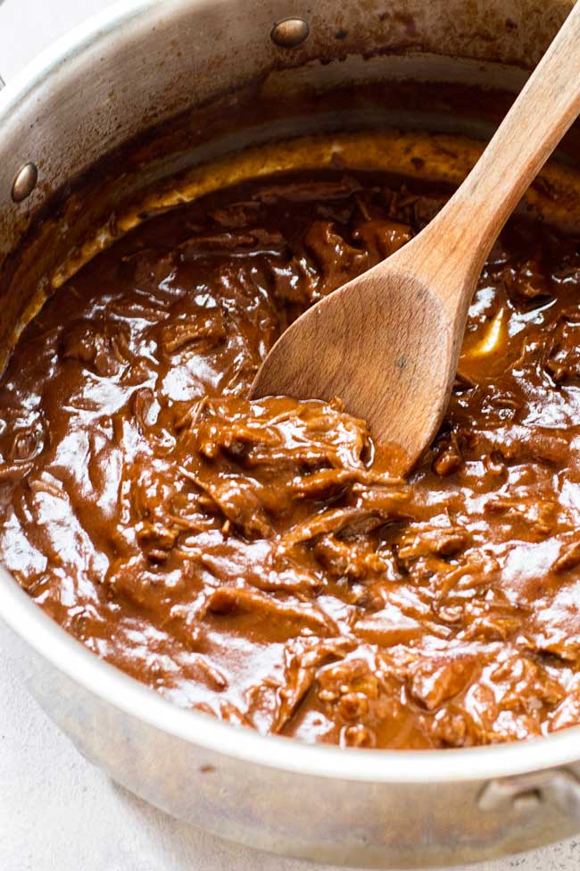 A pot of shredded short ribs in mushroom sauce with a wooden spoon