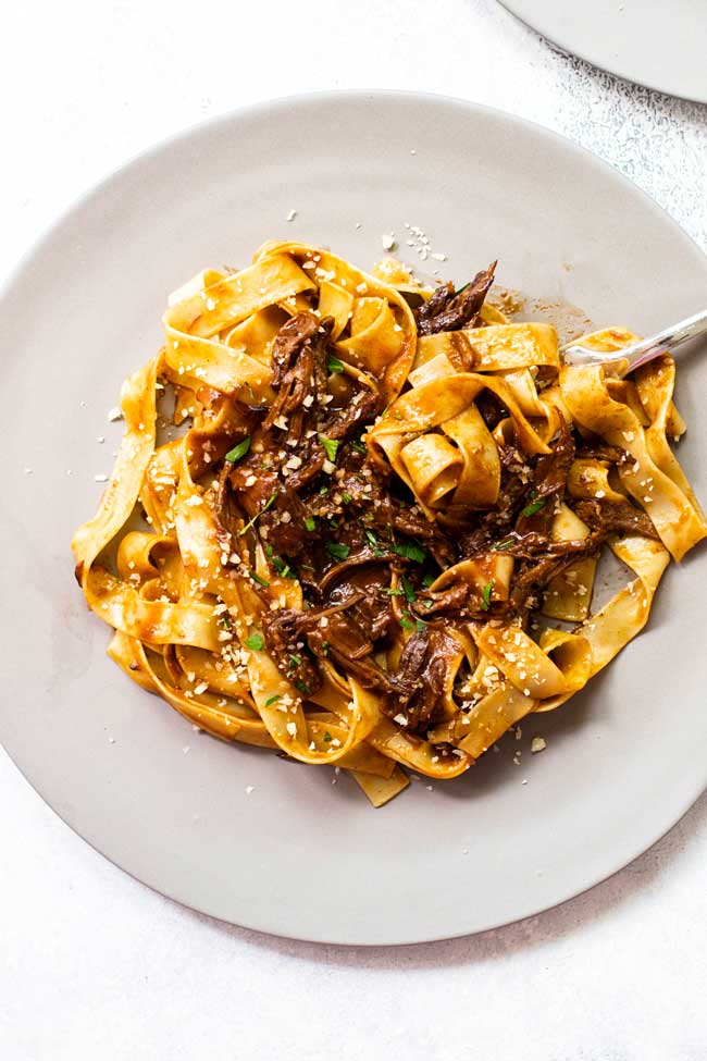 Pappardelle pasta on a gray plate topped with braised short rib muchroom sauce